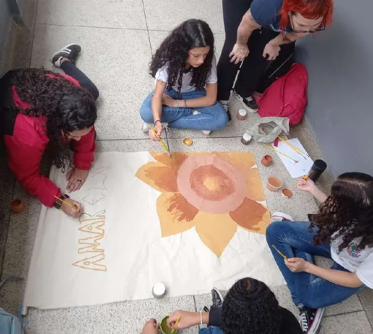 Estudantes sentados no chão pintando um sol em tinta de terra sobre papel