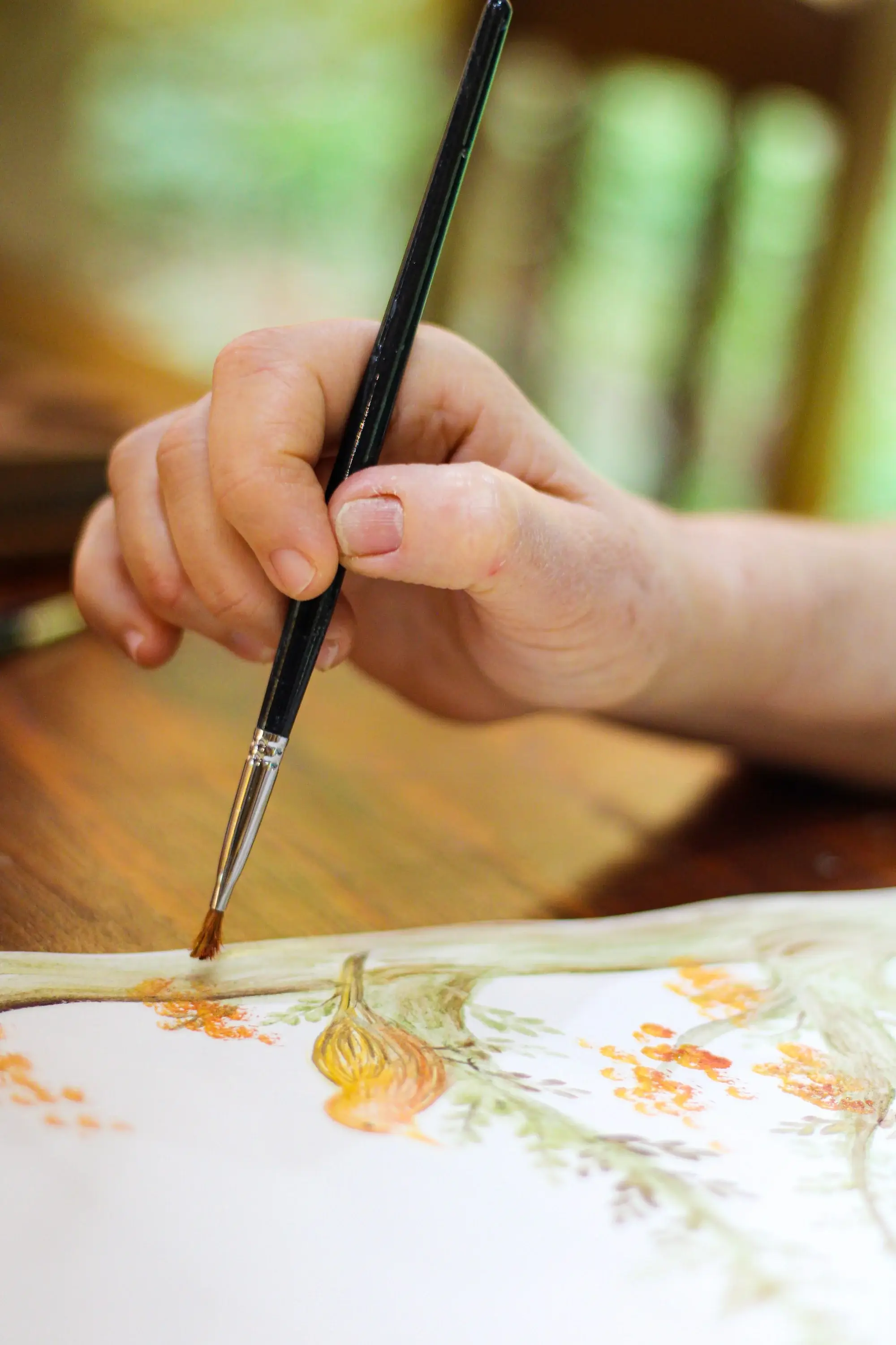 Pincel aplicando aquarela de terra em uma pintura botânica de flores alaranjadas