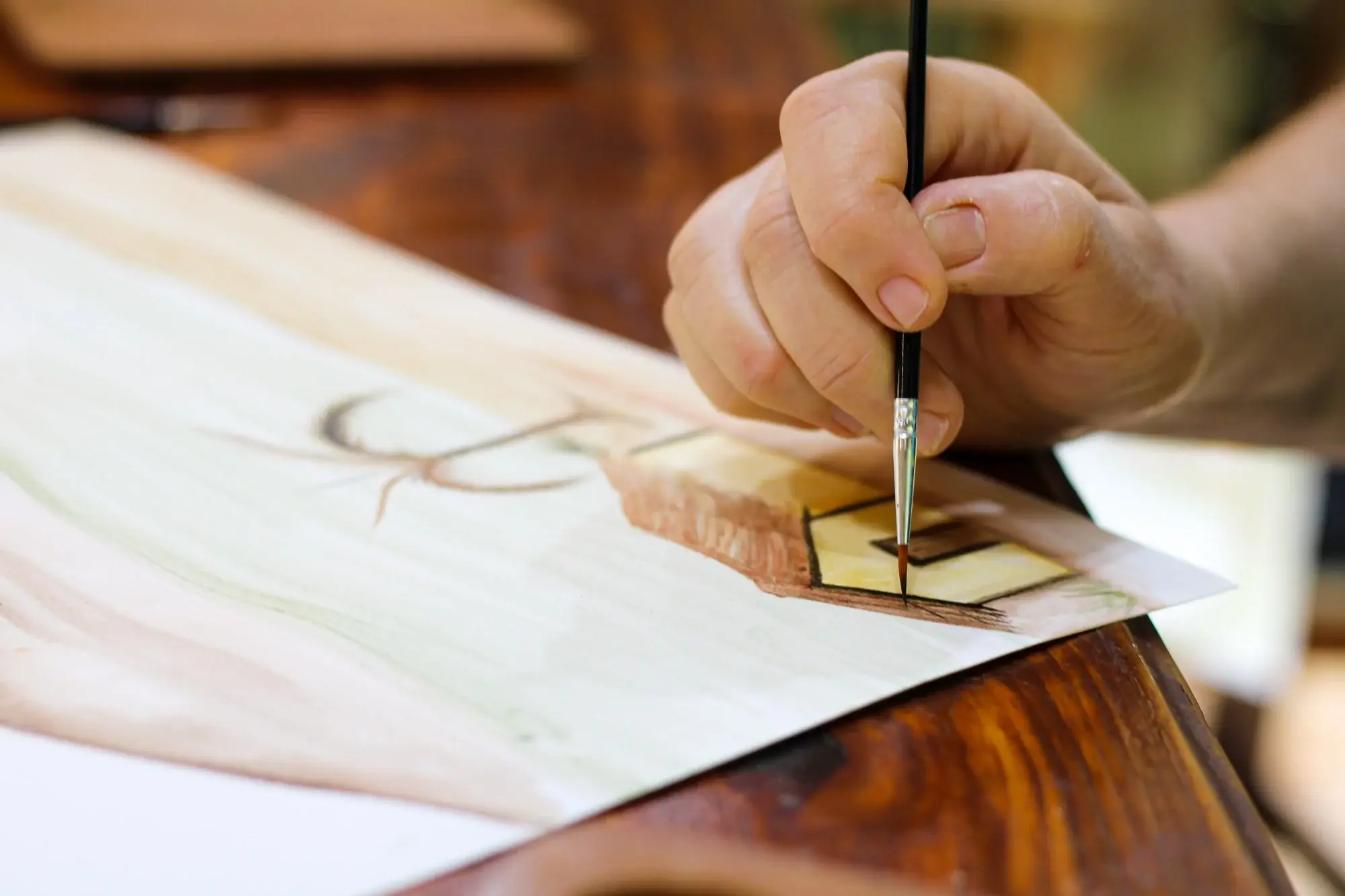 Mão pintando uma paisagem em aquarela de terra sobre papel, em tons de verde e ocre