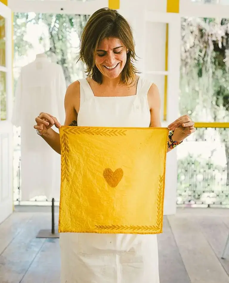 Lenço tingido de amarelo com estampa botânica de folhas e coração, segurado por participante da oficina