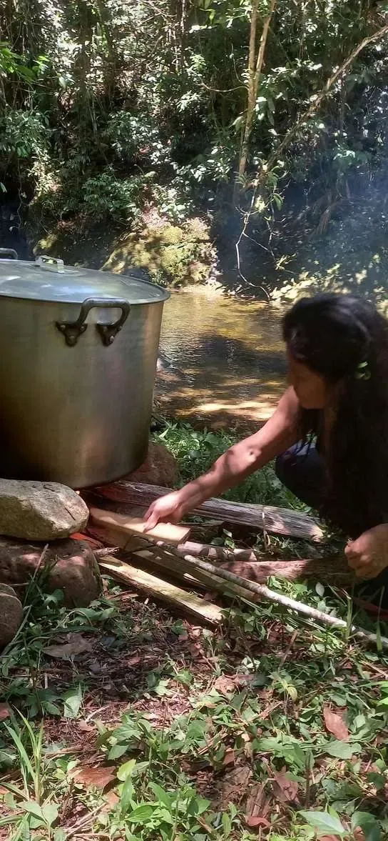 Panela de tingimento natural sobre fogo de lenha à beira do rio na mata